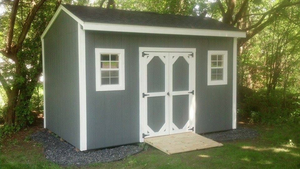 Gray shed with white trim, double doors, and a ramp, set in a yard.