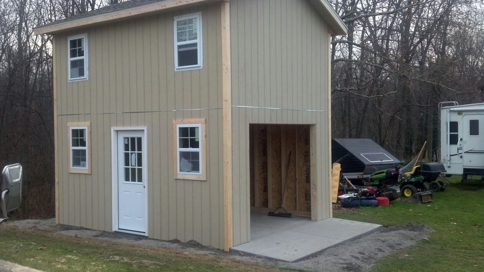 Two-story beige shed with a garage door and white trim and windows.