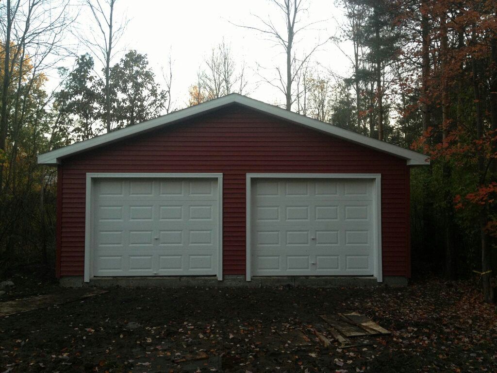 Red two-car garage with white garage doors, set against a backdrop of trees.