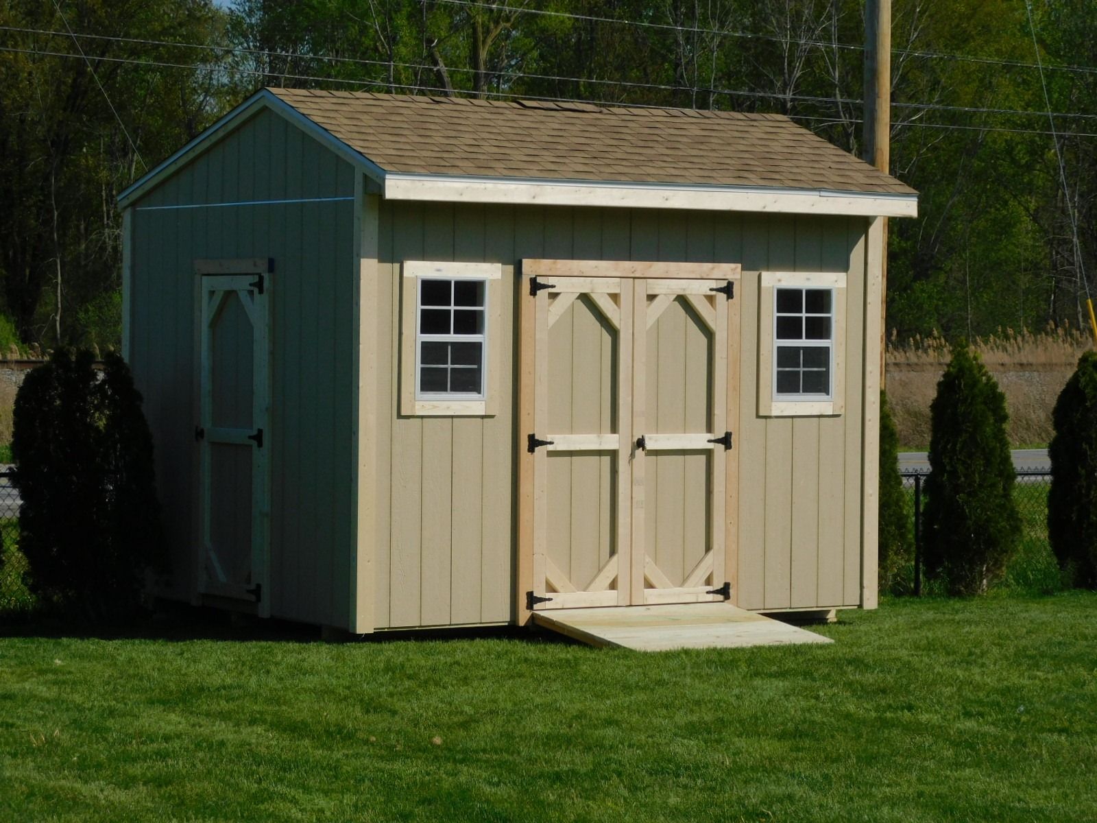 Tan shed with double doors, two windows, and a ramp, on green grass.