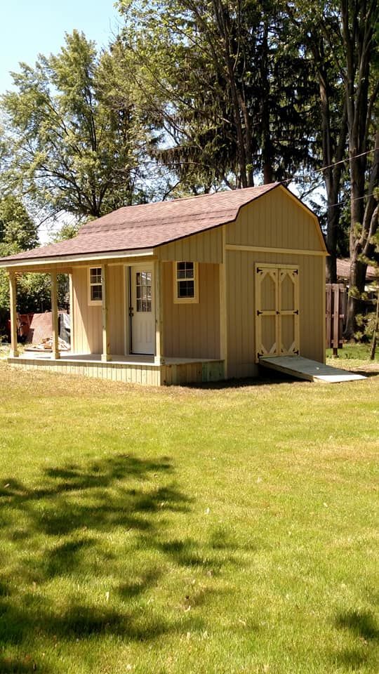 Tan shed with porch and ramp on green grass, trees in background.