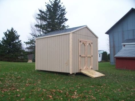 Tan shed with ramp on green lawn; other buildings in background.