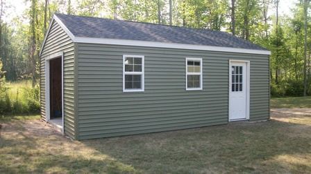 Green shed with garage door, windows, and white door in a grassy area.