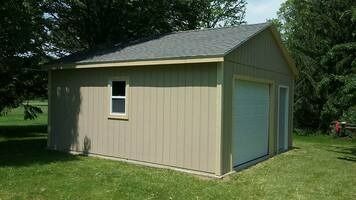 Tan garage with a gray roof and a white garage door, set in a grassy yard.