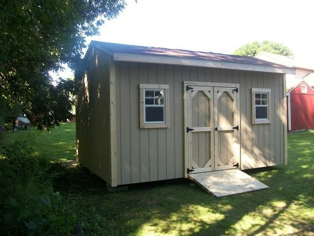 Tan shed with double doors, two windows, and a ramp, set in a grassy yard.