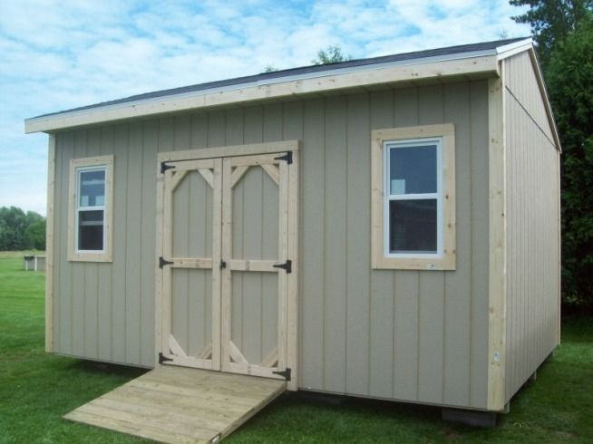 Tan shed with light wood trim and a ramp on green grass.