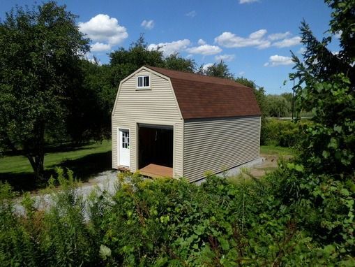 Tan shed with a brown roof and a small white door and window, set in a grassy yard.