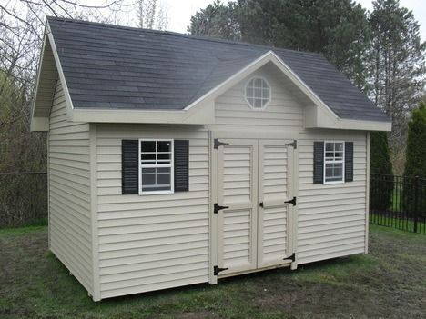 Tan shed with black shutters, roof, and door hardware, set in a grassy yard.