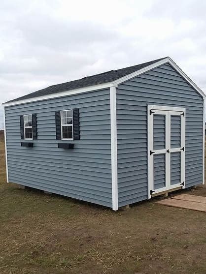Blue shed with white trim, two windows, black shutters, and double doors; outdoors.