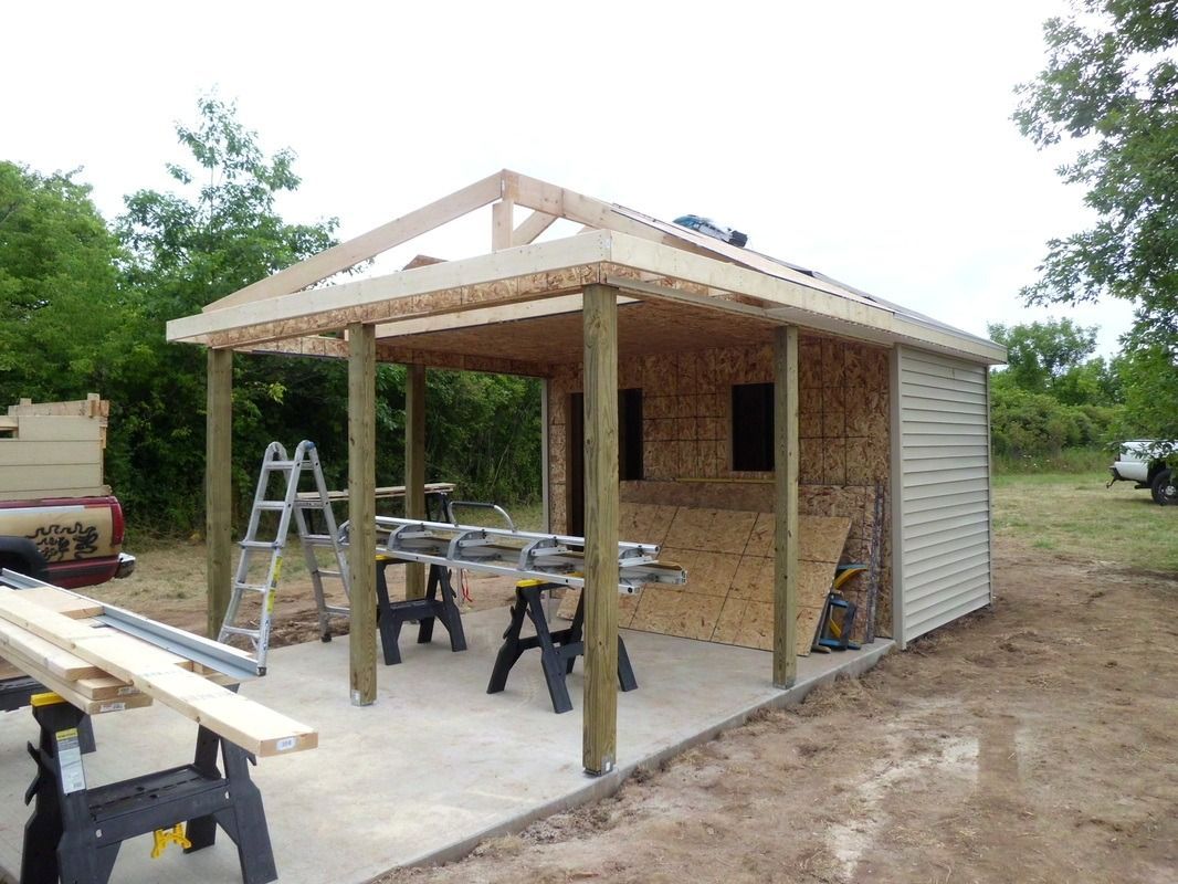 Shed under construction: wooden posts, roof framing, partially sided, concrete base, tools visible.