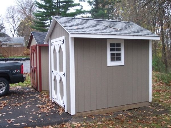 Two sheds: tan with white trim, a window, and doors; red shed in the background next to a black truck.