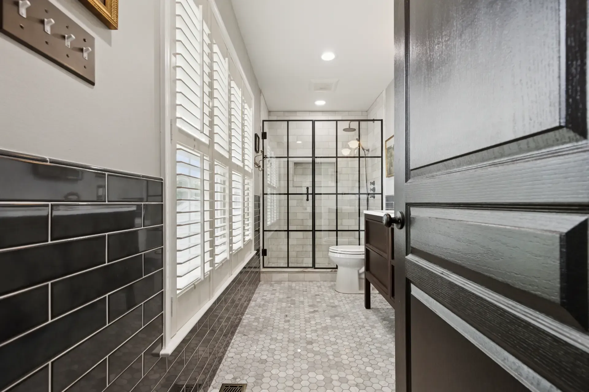 A bathroom with black tiles , a toilet , and a walk in shower.
