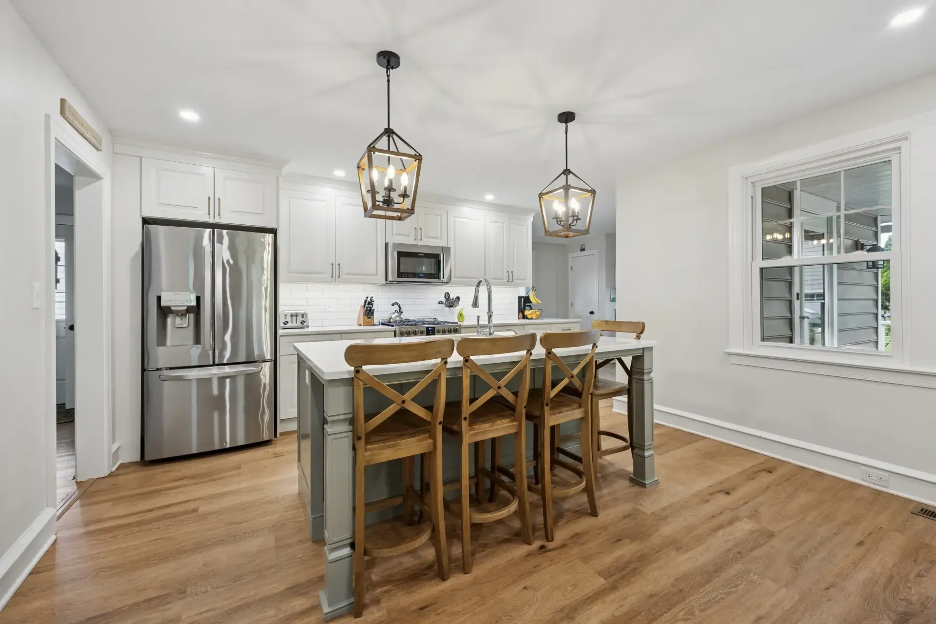 A kitchen with stainless steel appliances , white cabinets , hardwood floors and a large island.