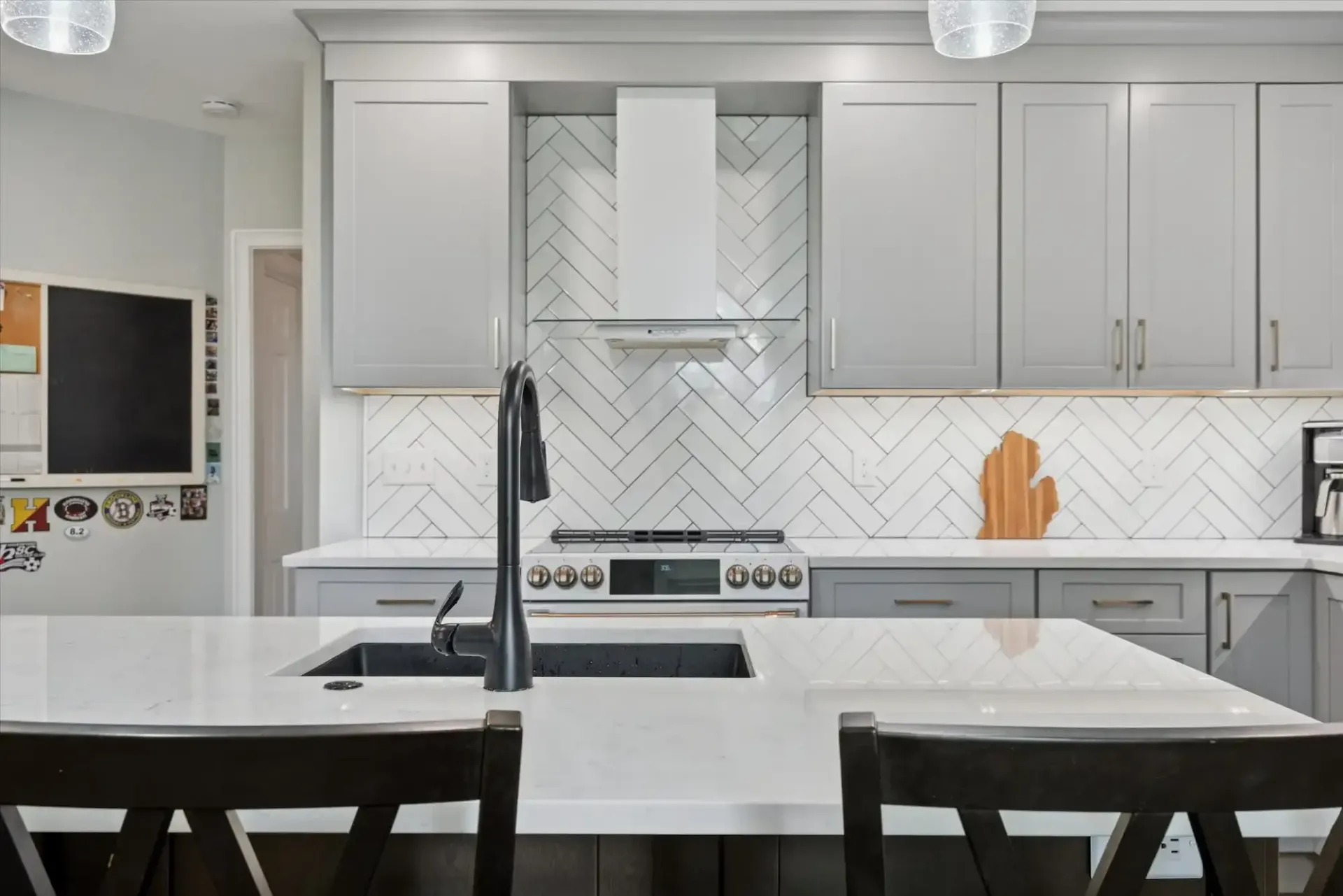A kitchen with gray cabinets , white counter tops , a sink , and a stove.