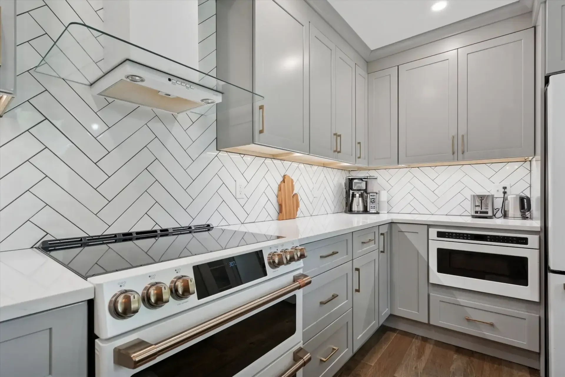 A kitchen with gray cabinets , a stove , a microwave and a refrigerator.