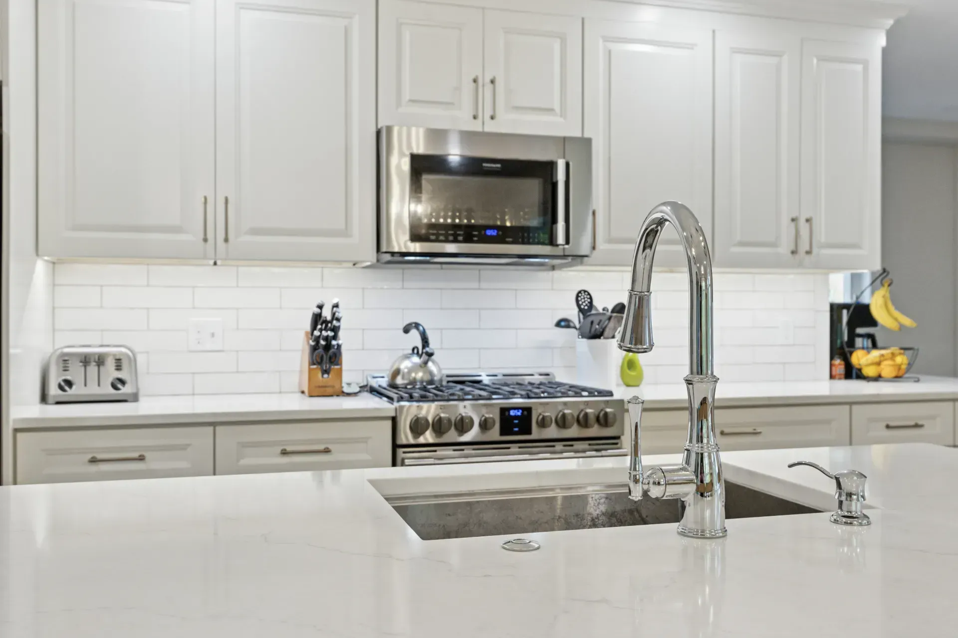 A kitchen with white cabinets , stainless steel appliances , a sink , stove and microwave.