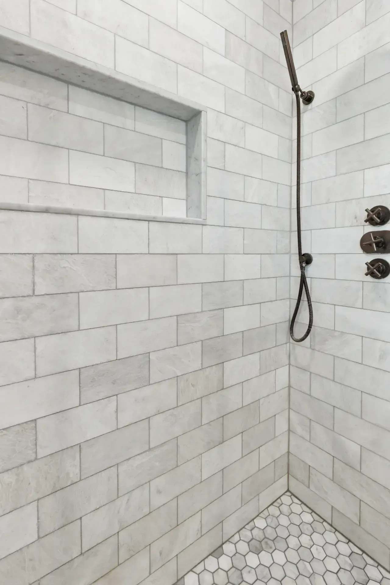 A shower with white tiles and a black shower head