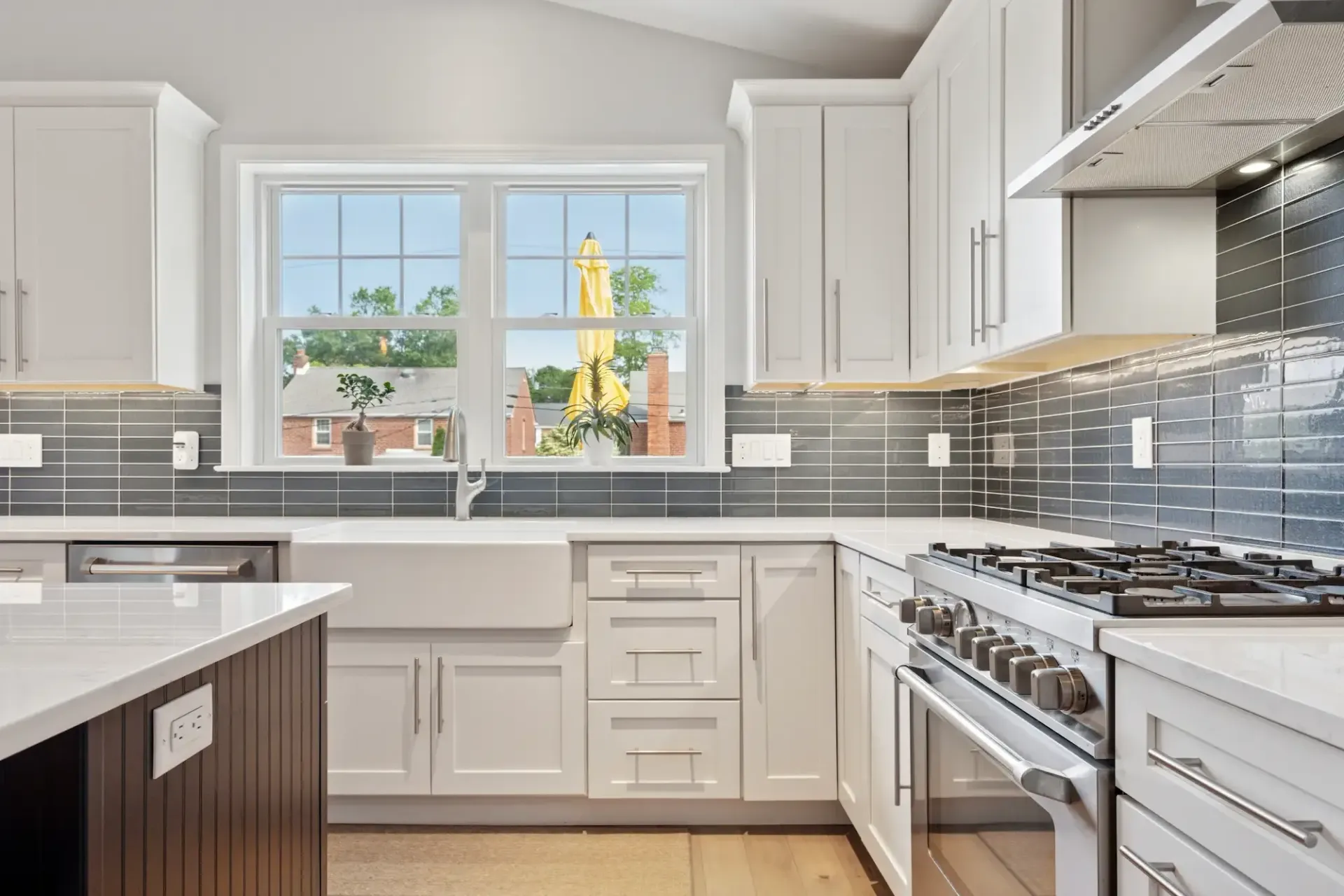 A kitchen with white cabinets , a stove , a sink , and a window.