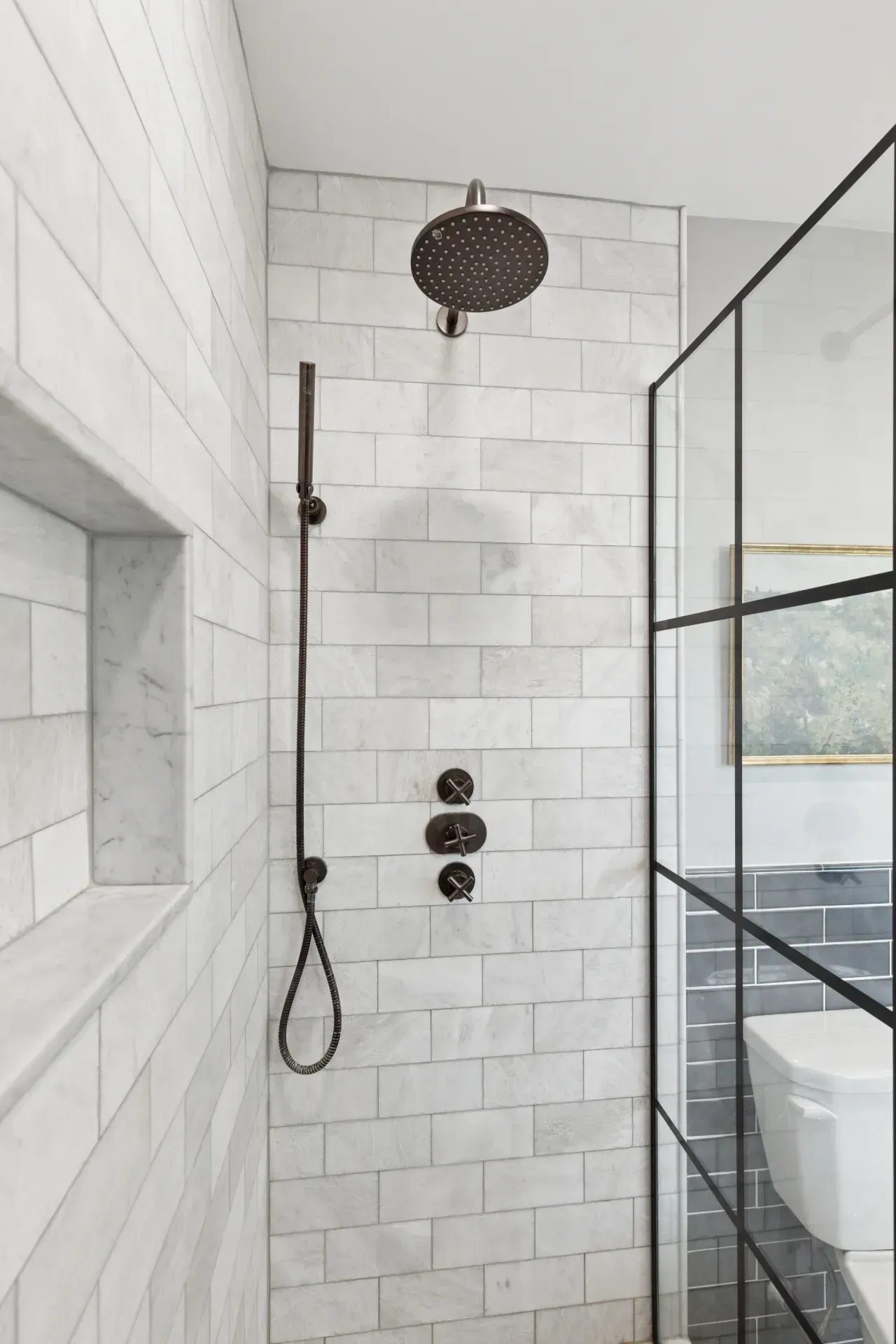 A bathroom with white tiles and a black shower head.