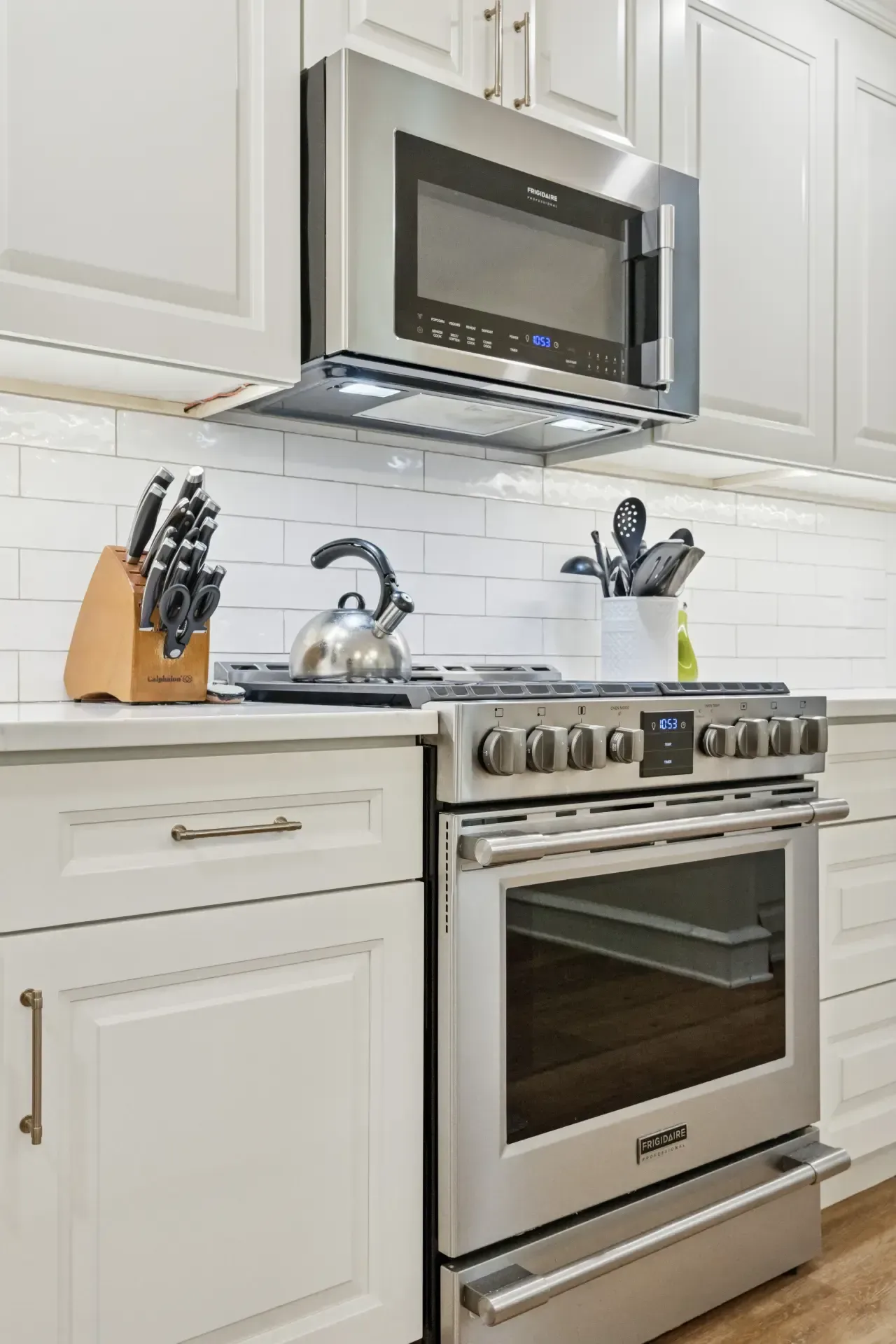 A kitchen with stainless steel appliances , white cabinets , a stove and a microwave.