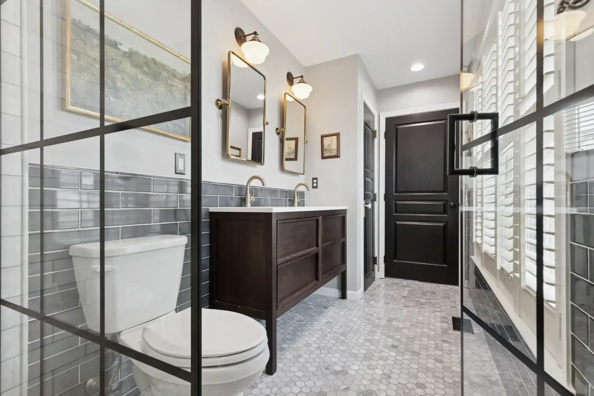 A bathroom with a toilet , sink , mirrors and shutters.