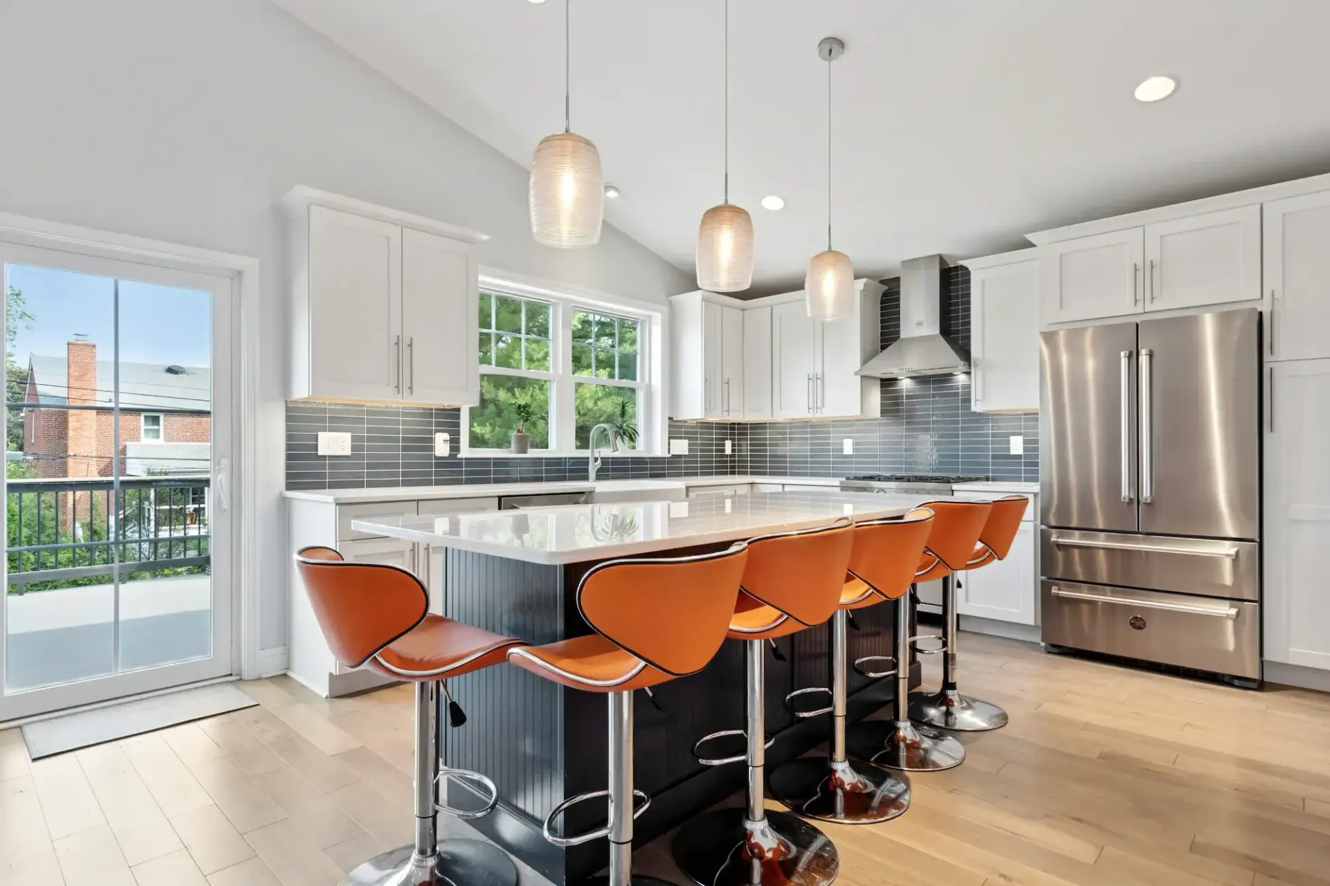 A kitchen with stainless steel appliances , white cabinets , a large island , and orange bar stools.