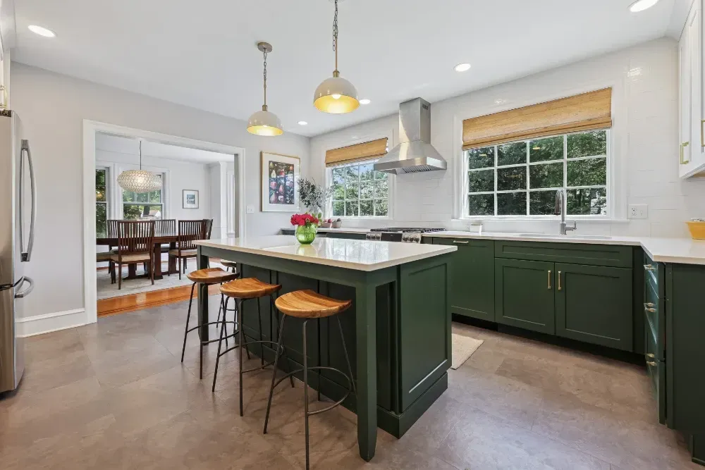A kitchen with green cabinets and stools and a large island.