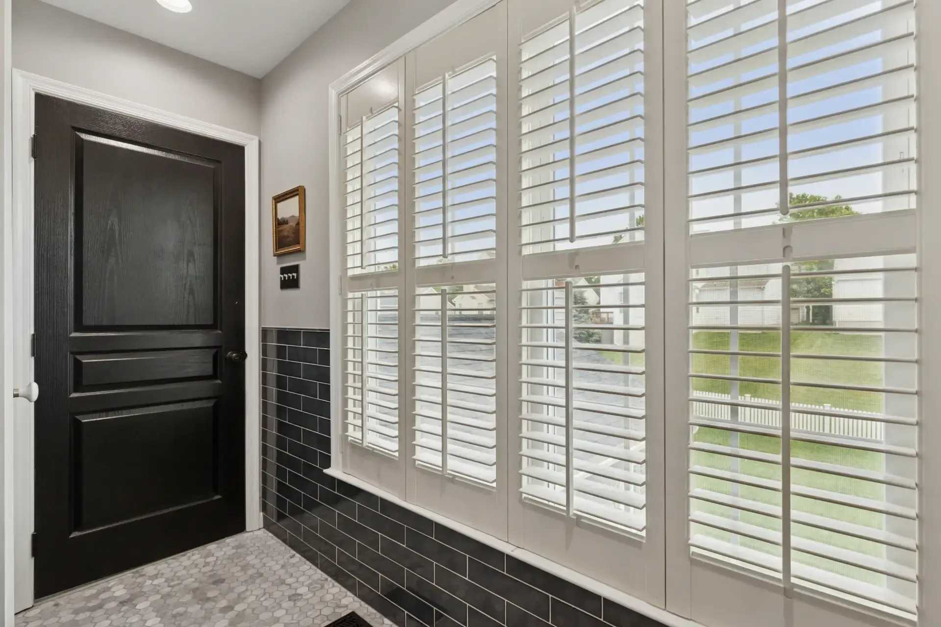 A hallway with shutters on the windows and a black door.