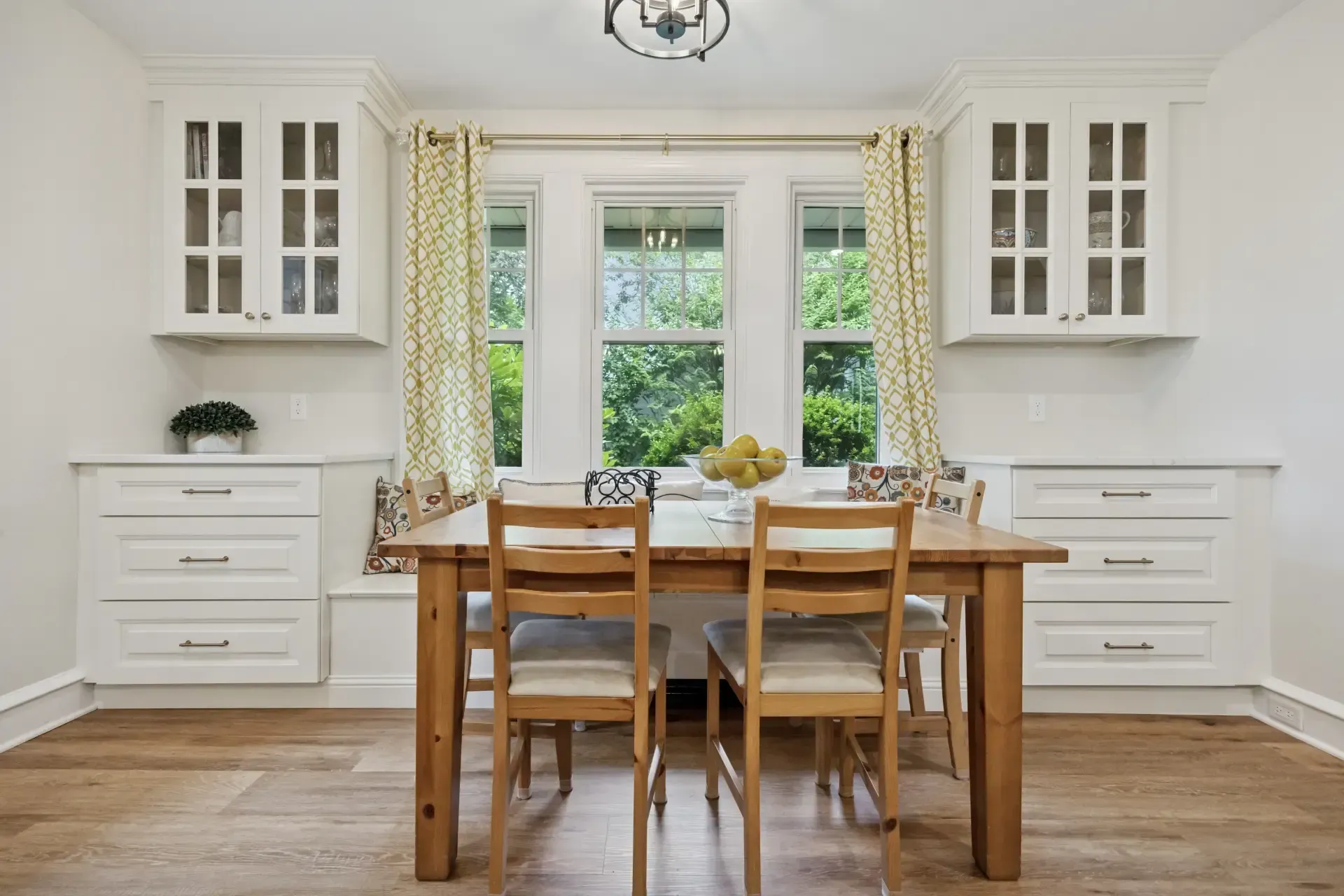 A dining room with a wooden table and chairs and white cabinets