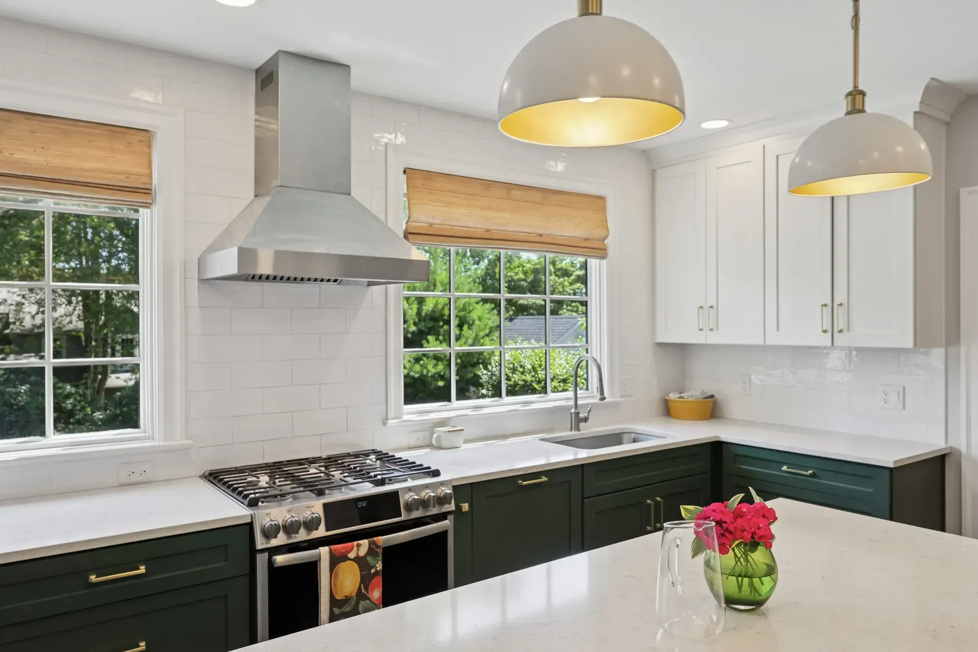 A kitchen with green cabinets , white counter tops , stainless steel appliances , and a large island.