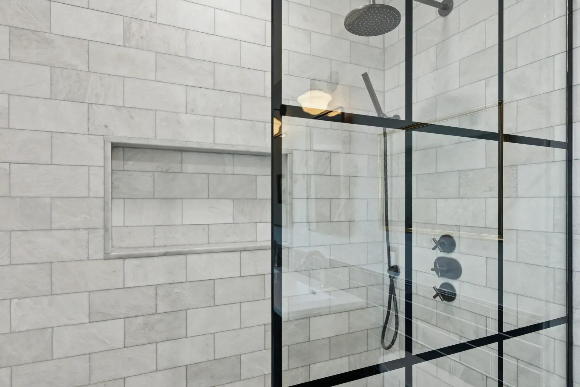 A shower stall with a black frame and white tiles.