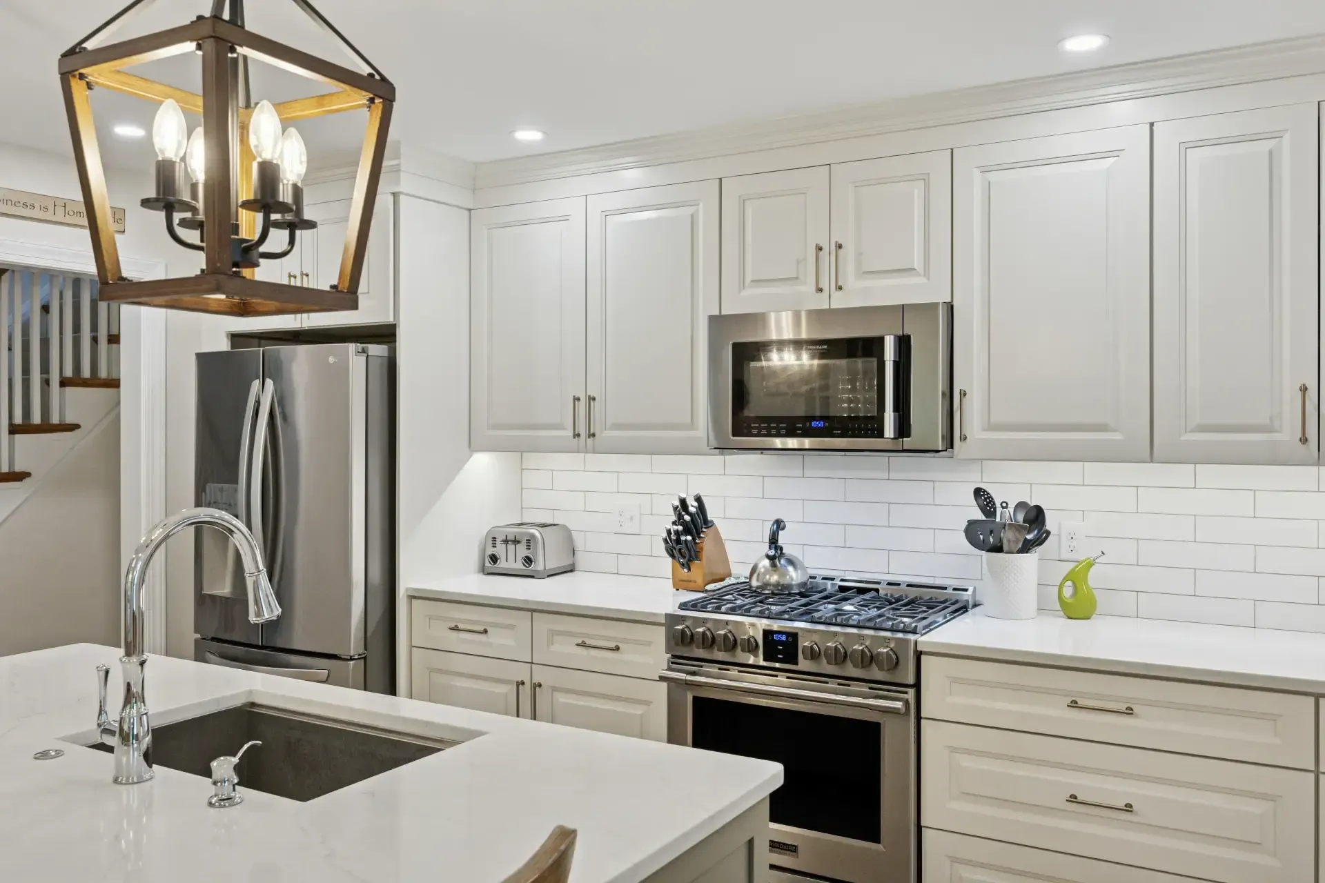 A kitchen with white cabinets , stainless steel appliances , a sink , and a chandelier.
