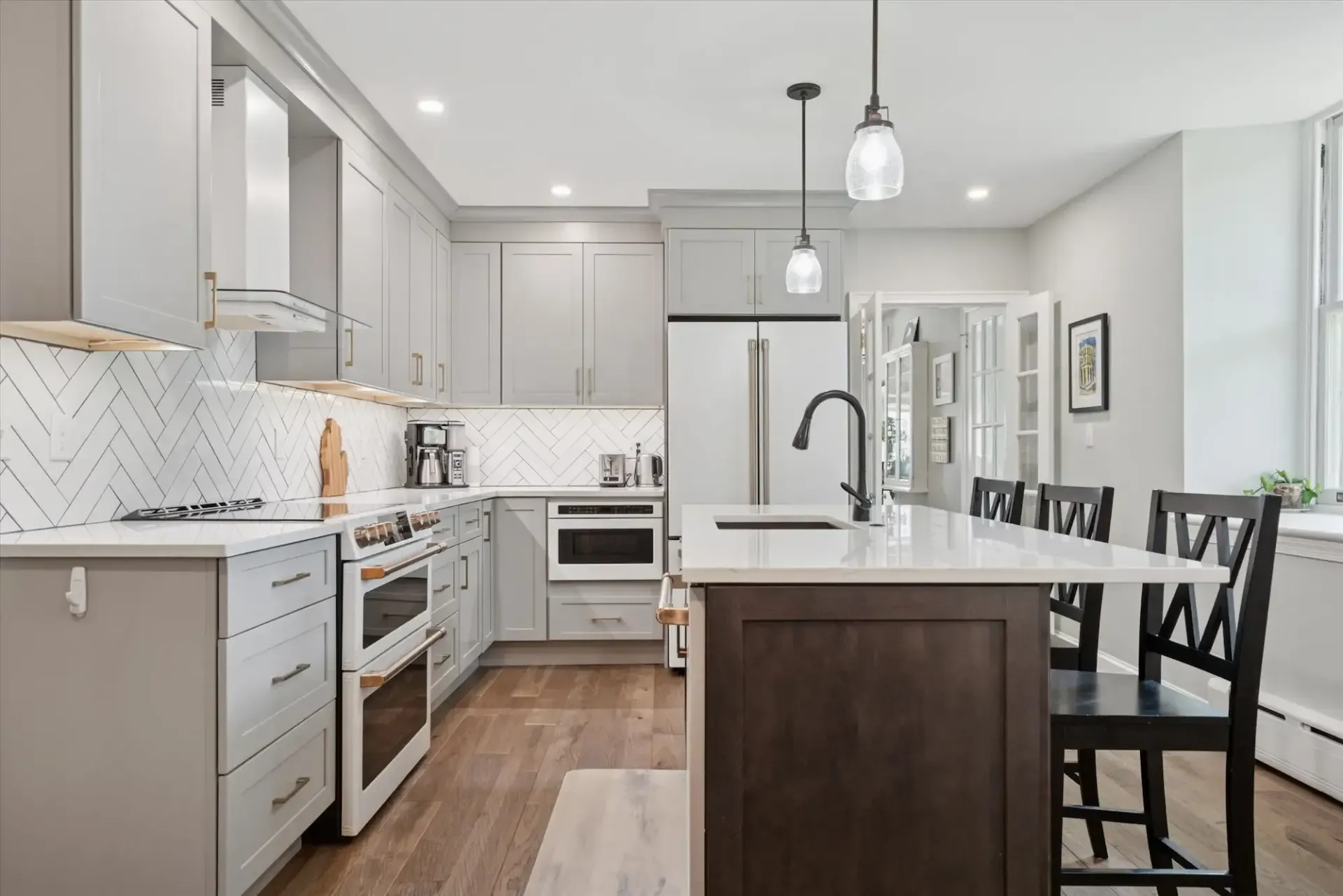 A kitchen with gray cabinets , white counter tops , stainless steel appliances and a large island.