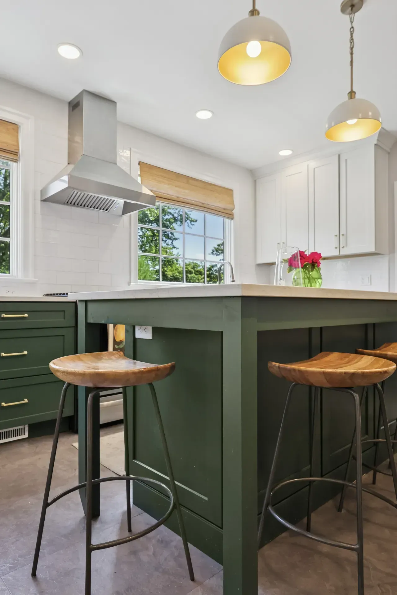 A kitchen with green cabinets and wooden stools and a large island.