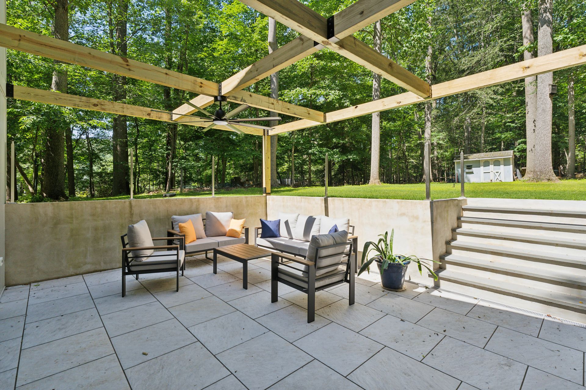 Outdoor patio with seating, a wooden pergola, and a forest backdrop.