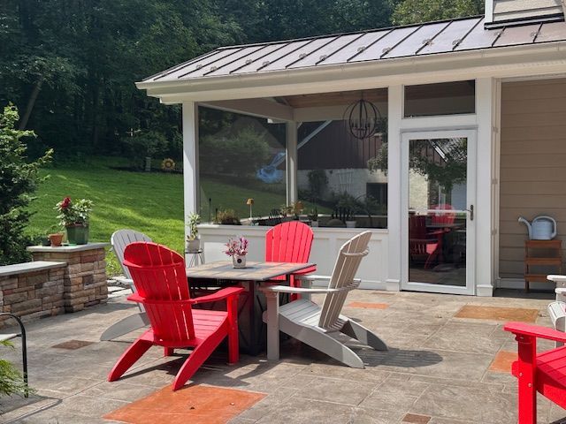 Patio with red and gray chairs around a table, with a screened-in porch and grassy backyard.