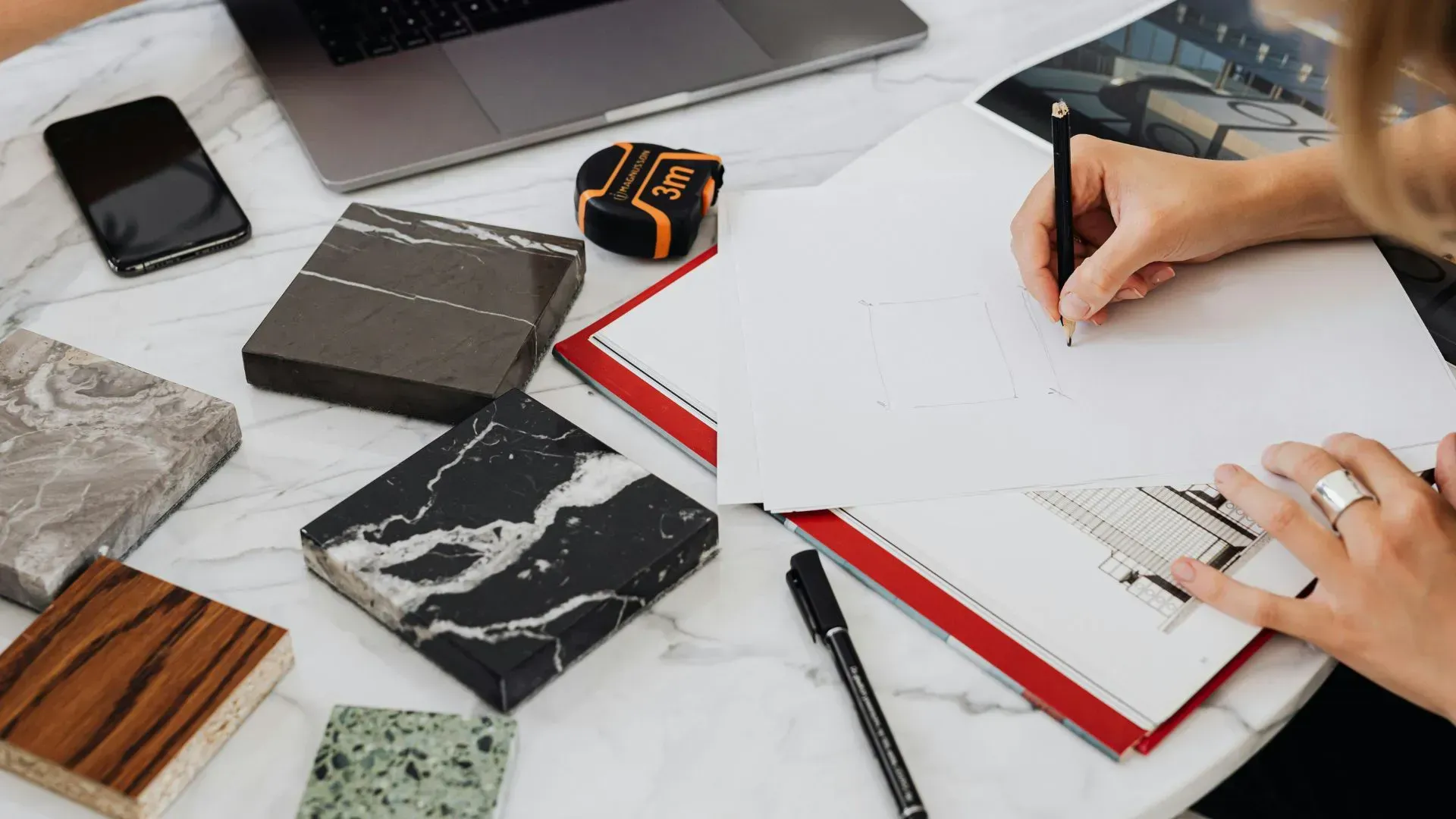 Hand writing in notebook with calculator and cash on a white table.