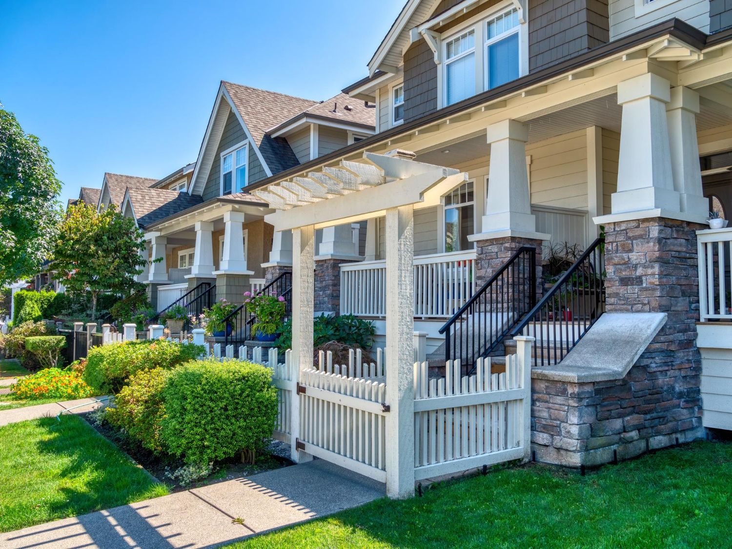 Row of townhouses with beige and brown exteriors, fronted by manicured lawns and a white picket fence.