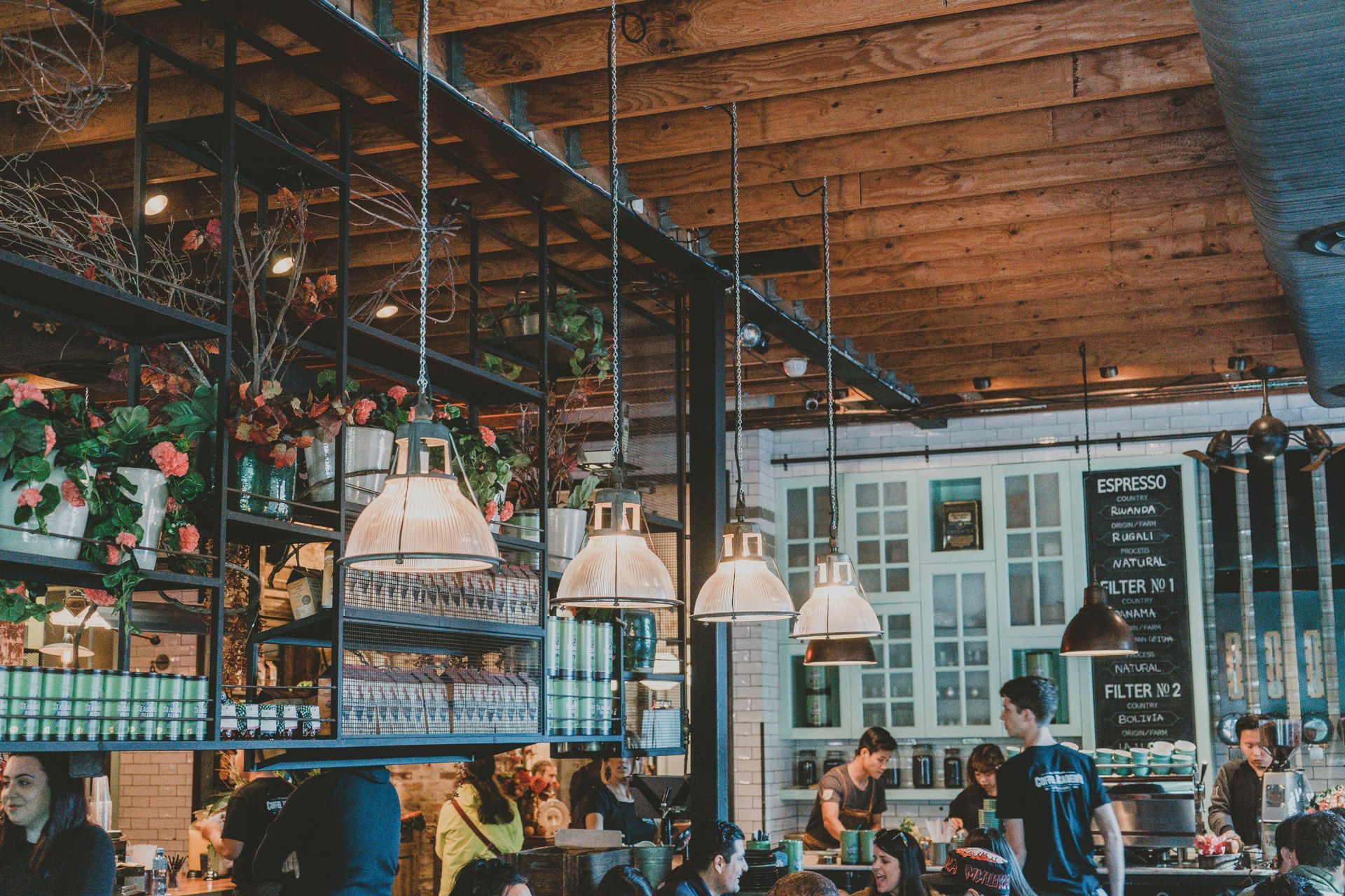 Restaurant interior with hanging lights, wooden ceiling, and people dining.