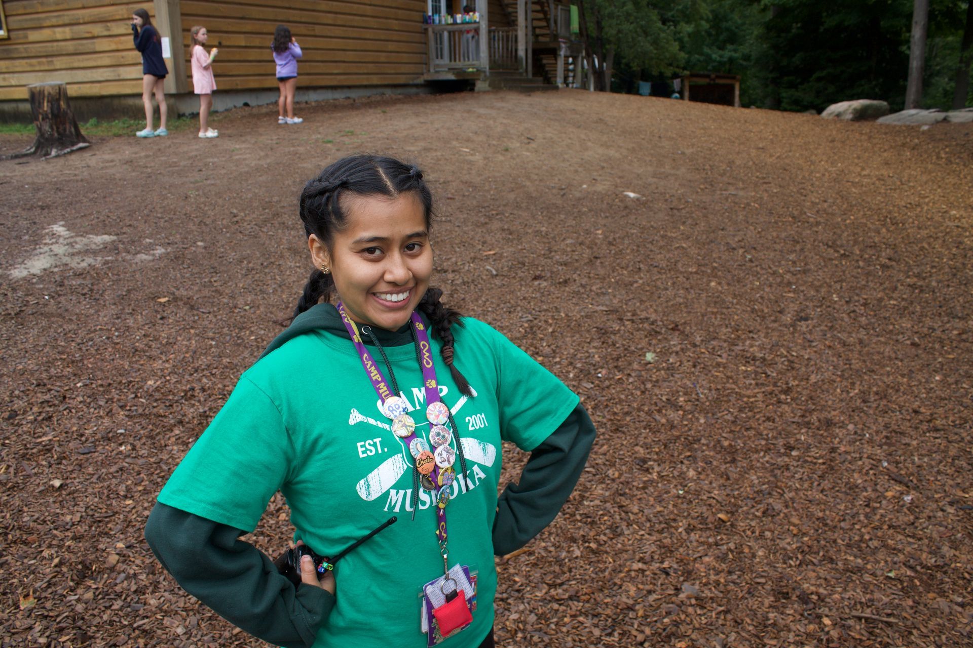 A girl in a green shirt is standing in a field with her hands on her hips.