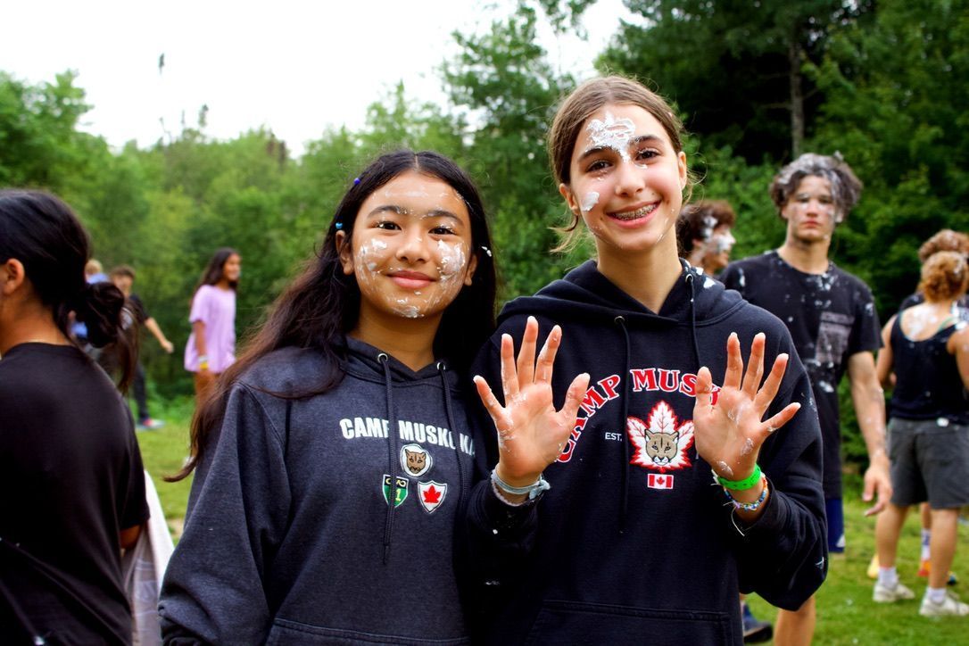 A girl with paint on her face is wearing a blue shirt that says camp mini girl