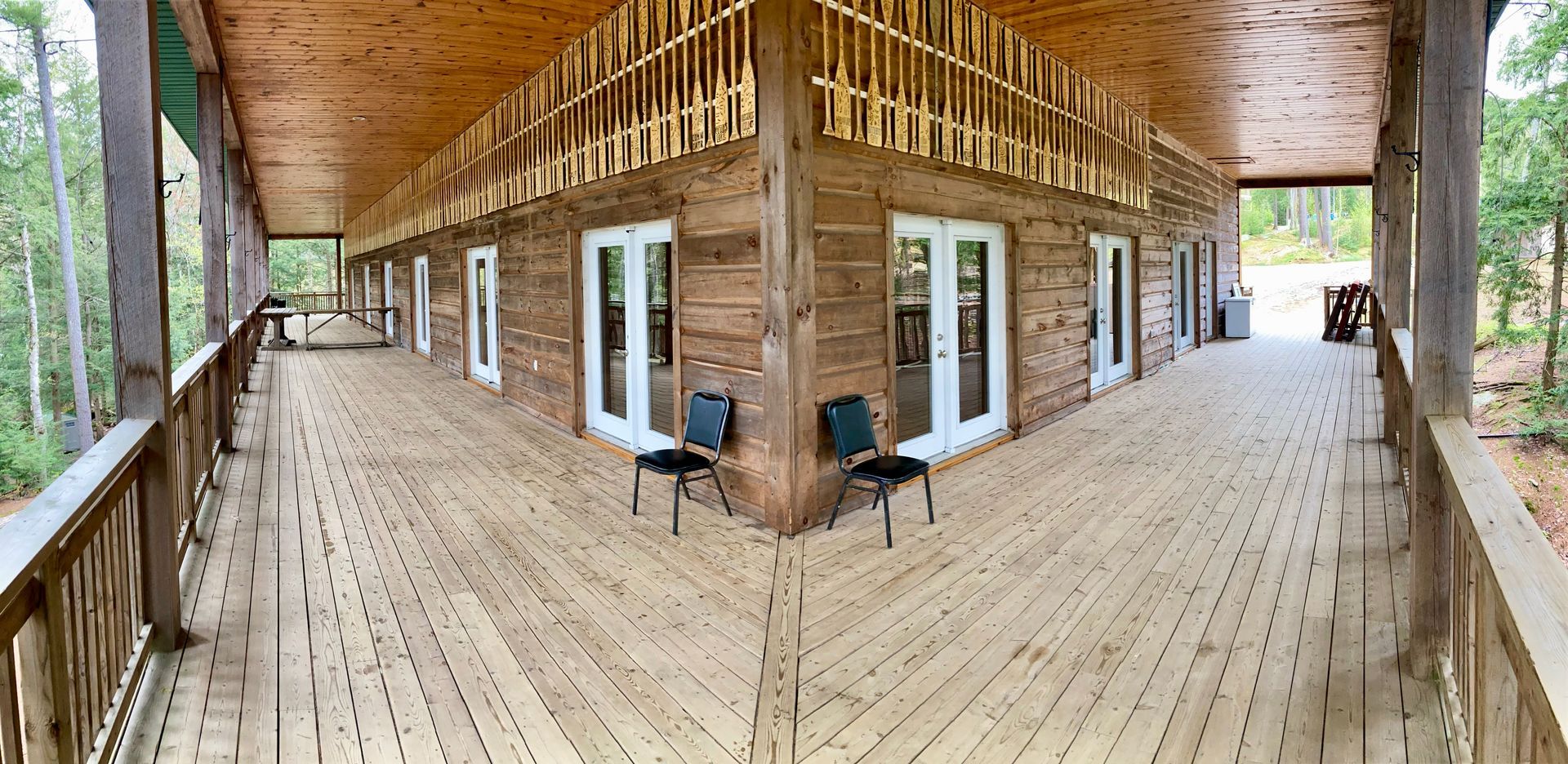 A large wooden deck with chairs on it is surrounded by trees.