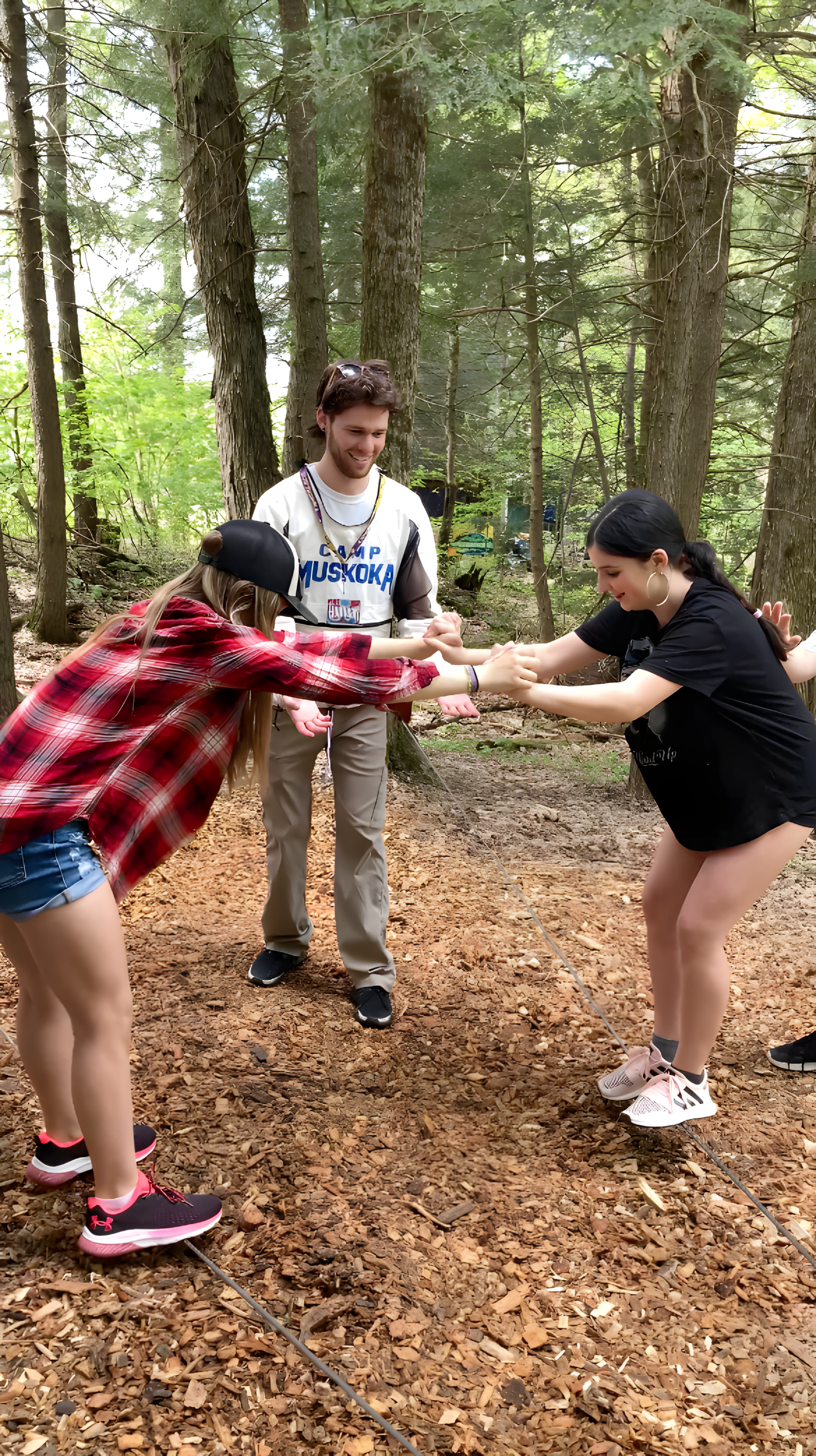 A group of people are standing in the woods holding hands trying to navigate a low ropes course.