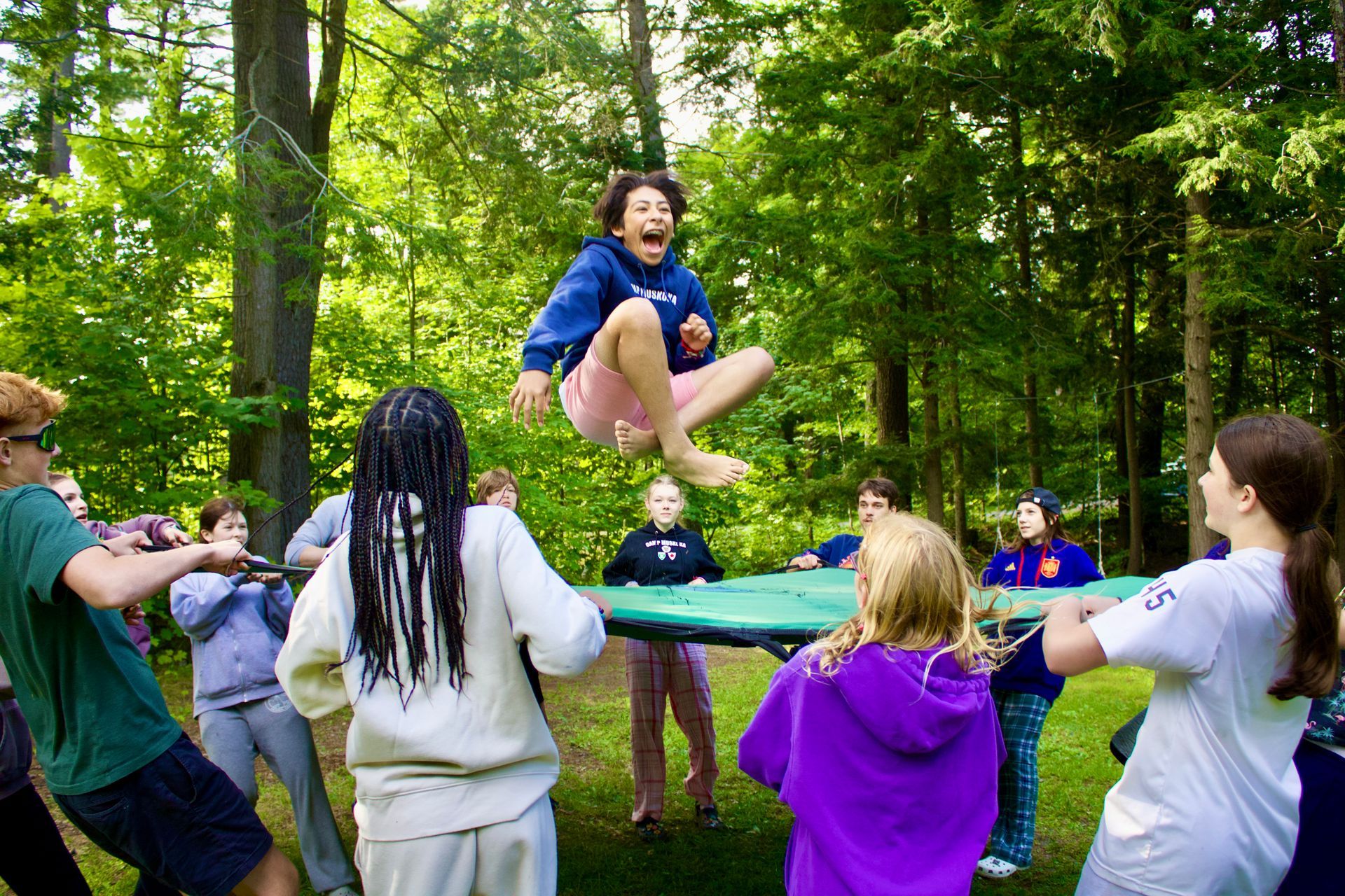 A group of children are playing with a trampoline in the woods.