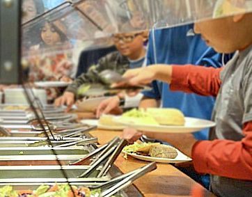 A boy is taking a plate of food from a buffet line.