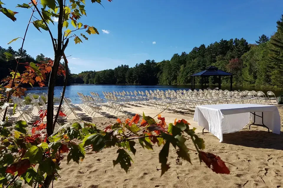 A table and chairs are set up on the beach near a lake.