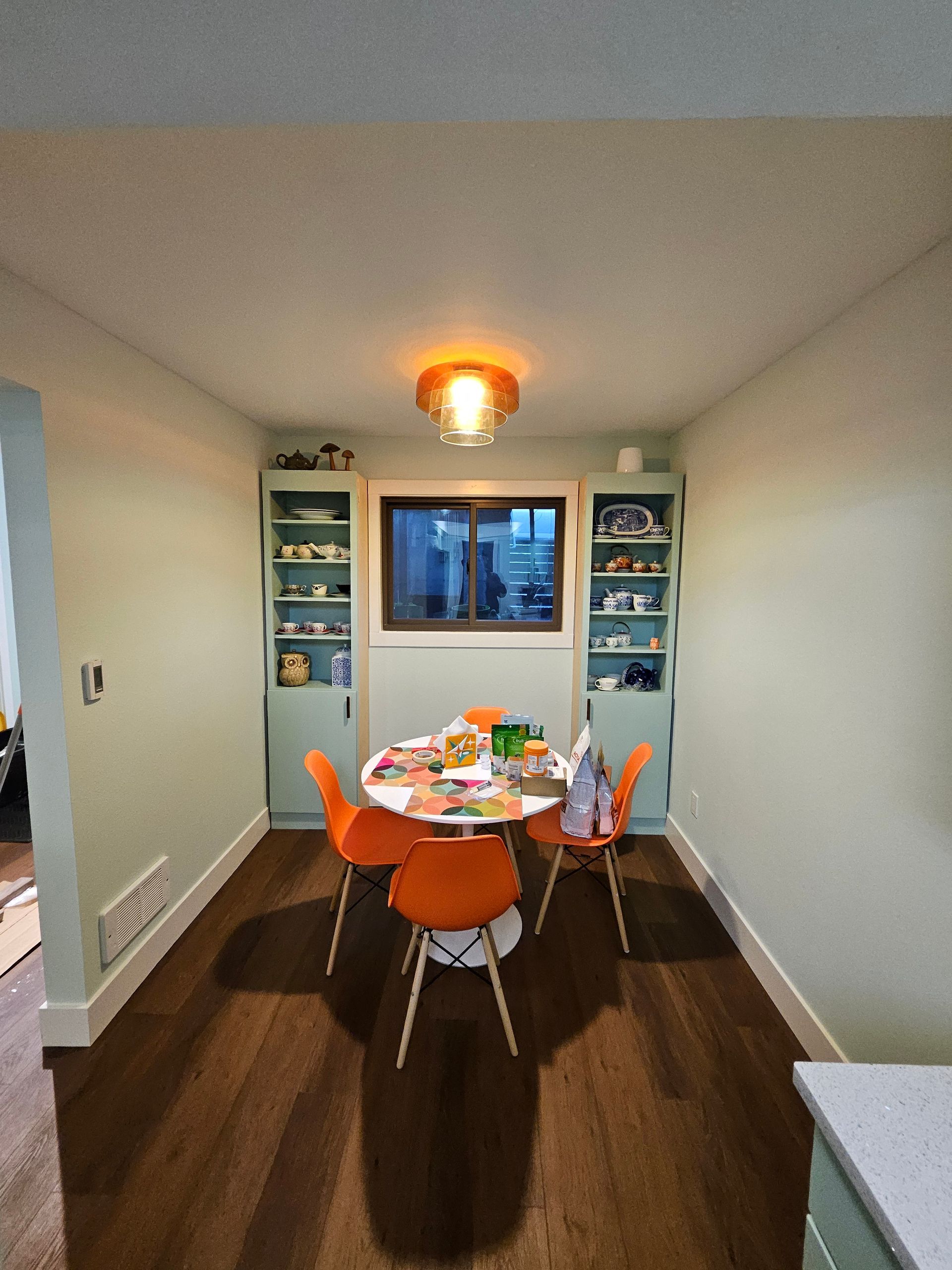 Small dining room with round table, orange chairs, built-in shelves, and a window.
