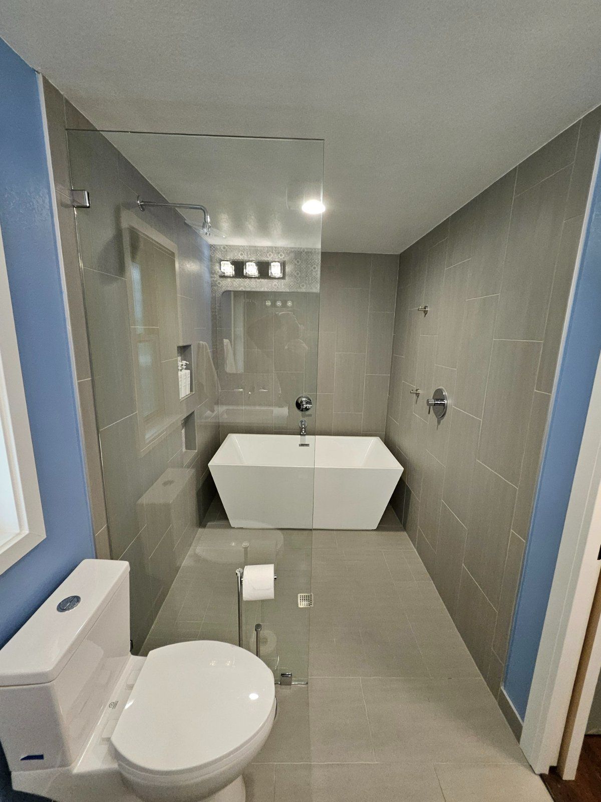 Modern bathroom with gray tiled walls, a white tub, and a glass shower.