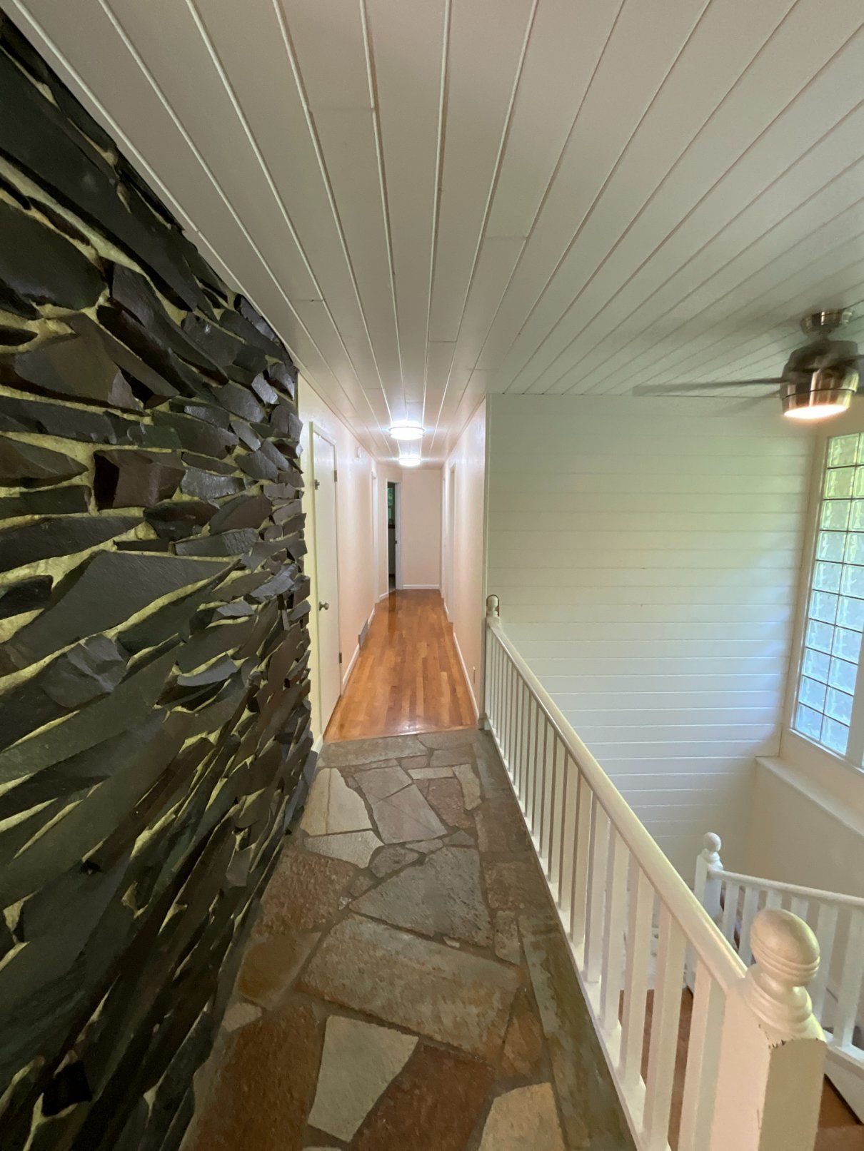 Hallway with stone wall and ceiling, wooden floor, and a staircase.