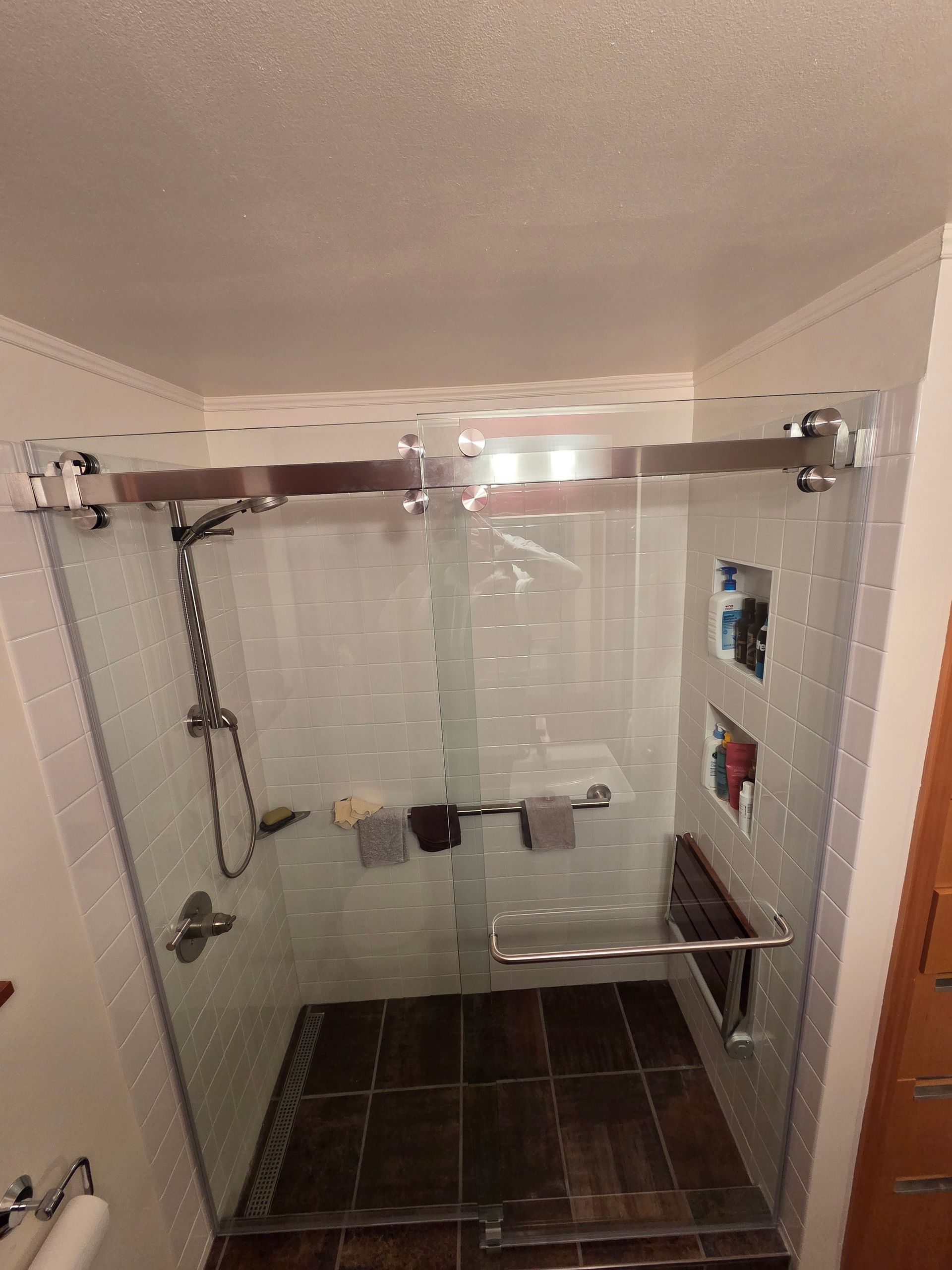 Glass shower enclosure with sliding door and chrome fixtures, on tiled floor.